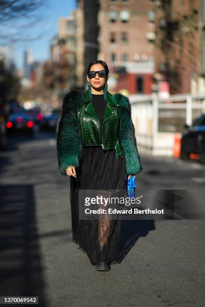 Samia Laaboudi wears sunglasses, green long fringed earrings, a black top, a green leather jacket with fluffy faux fur sleeves, a black ribbed top, a...