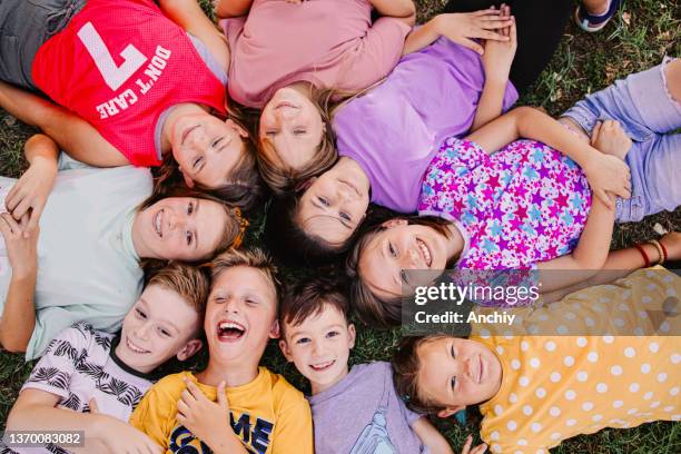 hochwinkelansicht einer gruppe von kindern, die sich hinlegen, während sie in die kamera lachen - ferienlager stock-fotos und bilder