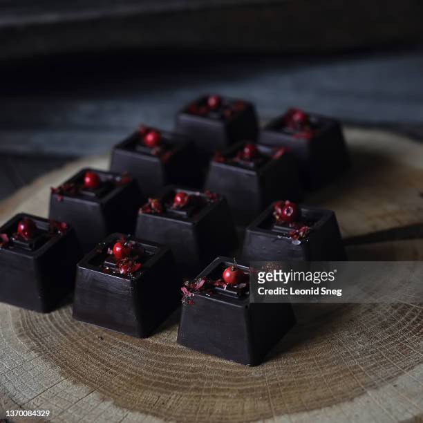 dark chocolate bonbons with pink pepper design side view on wooden cut background closeup. selective focus - praline stock pictures, royalty-free photos & images