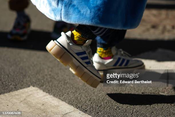 Guest wears yellow and green print pattern socks, a blue fluffy long oversized coat from Adidas, white matte leather and royal blue logo sneakers...