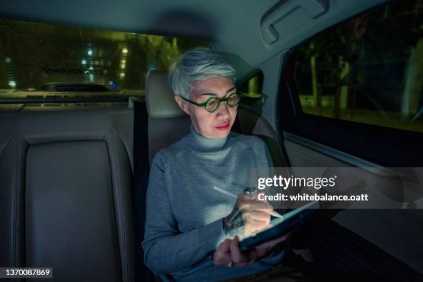 ältere frau mit smartphone im auto unter stadtlicht - management car smartphone stock-fotos und bilder