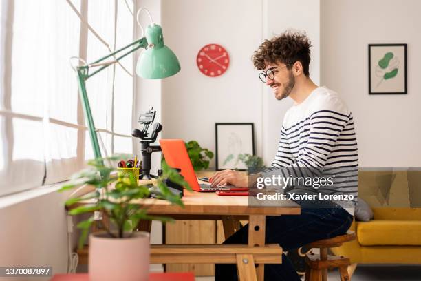 young hipster man working on laptop while sitting at desk at home. - homeoffice stock-fotos und bilder