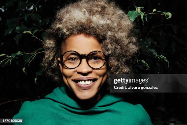 afro latin woman looking at camera and smile while standing with green plants on background. - flora gonzalez bildbanksfoton och bilder