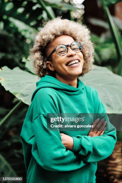 afro woman laughing while standing with her arms crossed on a green natural background. - man expressive background glasses stock-fotos und bilder