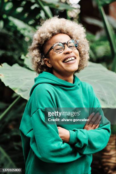 afro woman laughing while standing with her arms crossed on a green natural background. - environmental conservation fotografías e imágenes de stock