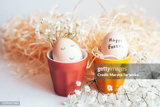 easter eggs with an inscription in colorful stands on a white background. easter. easter egg with stand. white gypsophila. happy easter. easter preparation. easter eggs. easter decor. multicolored egg cups. - chicken decoration stock-fotos und bilder