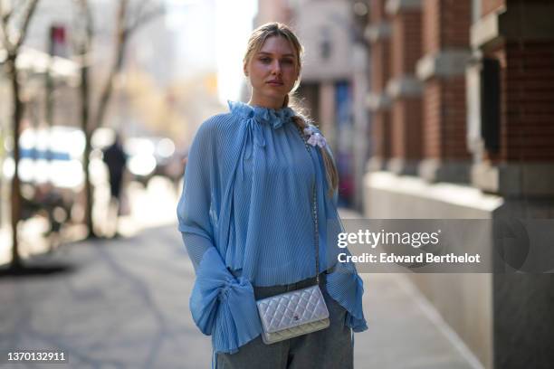 Guest wears a white Dior ribbon in the hair, a pale blue pleated / ruffled high collar long puffy sleeves blouse / shirt, a silver shiny leather WOC...