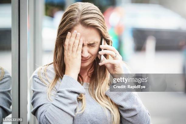 beautiful woman in her 30s covers her face and cries as she talks on her cellphone in a city street - crying woman stock pictures, royalty-free photos & images