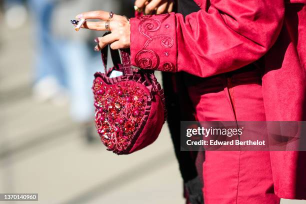 Guest wears a red with embroidered pattern collar jacket coat, silver rings, a burgundy ruffled shiny leather with red embroidered pearls / sequins...