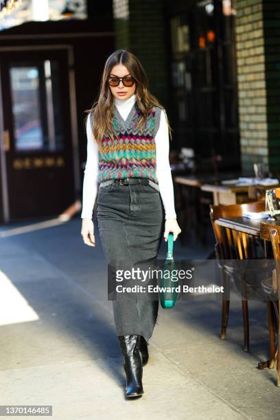 Guest wears black sunglasses, a white turtleneck pullover, a gray with green / yellow / black / pale purple / red print pattern V-neck / sleeveless...