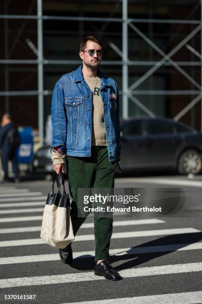 Guest wears sunglasses, a brown wool pullover with dark green print pattern, a blue denim jeans pants, dark green ribbed velvet pants, silver rings,...