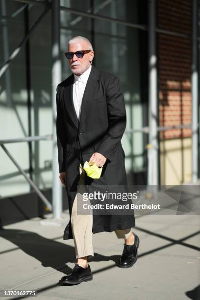 Guest wears sunglasses, a white shirt, a black striped long blazer jacket coat, beige suit pants, black shiny leather derbies shoes, outside New York...