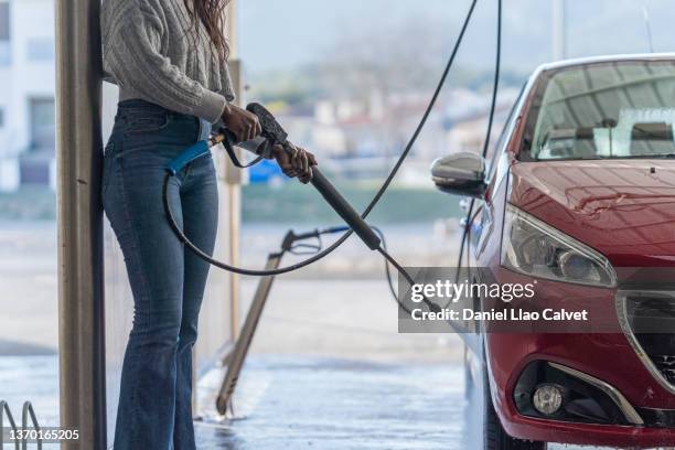 unrecognizable female in casual clothes  washing her r car with water gun - splash wasser stockfoto's en -beelden