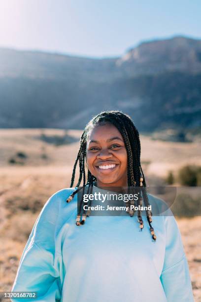 cute joyful headshot portrait of a cheerful young african american woman standing on a footpath outdoors while getting some exercise in a desert recreational area near the colorado national monument - braided stock pictures, royalty-free photos & images