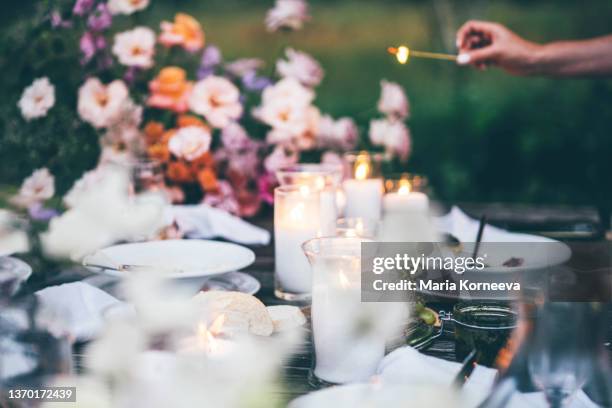 women ignite fire to decorative candles in stylish glass holders with thin wooden sticks at rustic table with elegant setting in garden closeup. - romantic picnic stockfoto's en -beelden