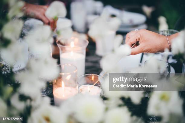 women ignite fire to decorative candles in stylish glass holders with thin wooden sticks at rustic table with elegant setting in garden closeup. - wedding table setting imagens e fotografias de stock