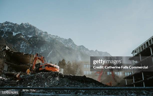 construction scene with a large digger against a blue sky and mountains - baustelle bagger stock-fotos und bilder