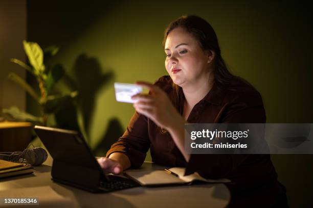 hermosa mujer de negocios de talla grande que compra en línea con su tarjeta de crédito desde casa por la noche - chubby credit fotografías e imágenes de stock
