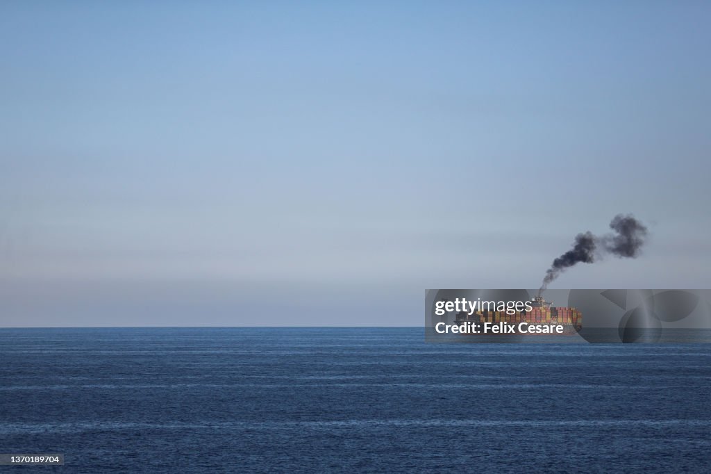 A large cargo ship in the distance smoking black fumes.