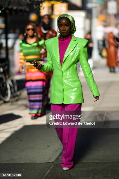 Guest wears a green shiny scarf on the head, a pink purple high neck pullover, matching pink purple large wide-legs suit pants, a green shiny...
