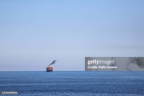 a large cargo ship in the distance smoking black fumes. - 貿易戰 個照片及圖片檔