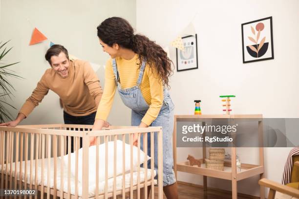 portrait of a happy couple preparing a crib for their soon to come baby - baby shower party stock pictures, royalty-free photos & images