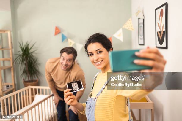 happy young couple taking a selfie with an ultrasound image of their baby to come - happy couple using cellphone stockfoto's en -beelden