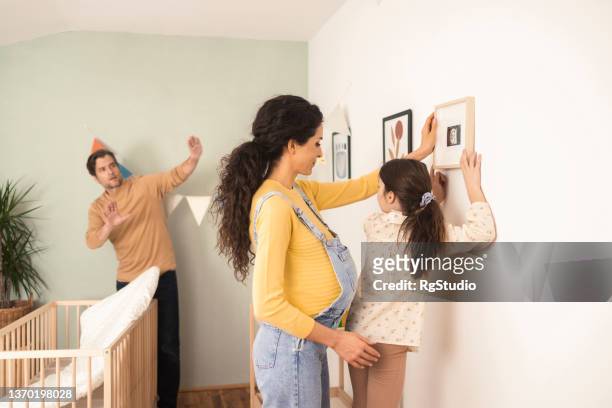 happy family arranging a room for the baby they're expecting - hanging photos stock pictures, royalty-free photos & images