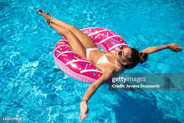 a beautiful girl in an inflatable donut is having fun in the pool - women's swimwear stock pictures, royalty-free photos & images