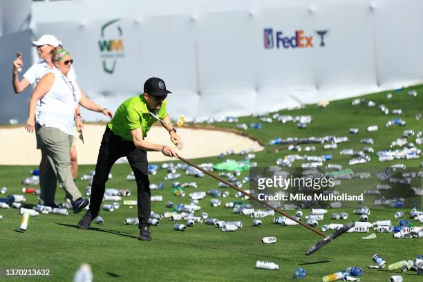 Groundskeepers pick up bottles thrown from the stands on the 16th hole after a hole-in-one by Sam Ryder of the United States during the third round...