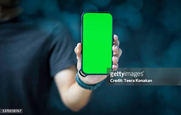 businessman holding a smartphone with a green blank screen - chroma key stock-fotos und bilder