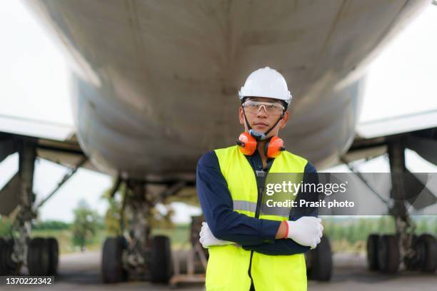 asian man engineer maintenance airplane holding white helmet in front airplane from repairs, fixes, modernization and renovation in airport."n - aerospace engineering stock pictures, royalty-free photos & images