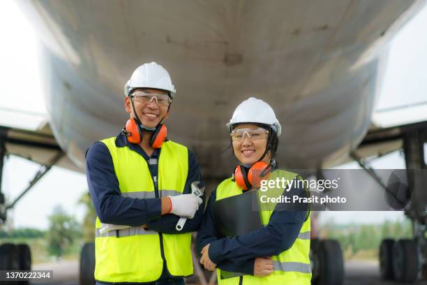 asian man and woman engineer maintenance airplane arm crossed and holding wrench in front airplane from repairs, fixes, modernization and renovation in airport."n - aerospace engineering stock pictures, royalty-free photos & images