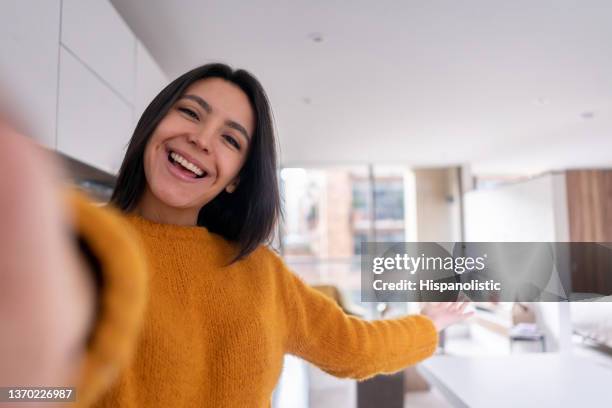beautiful young woman on a video call showing off her new home facing camera smiling - ado latino stock pictures, royalty-free photos & images