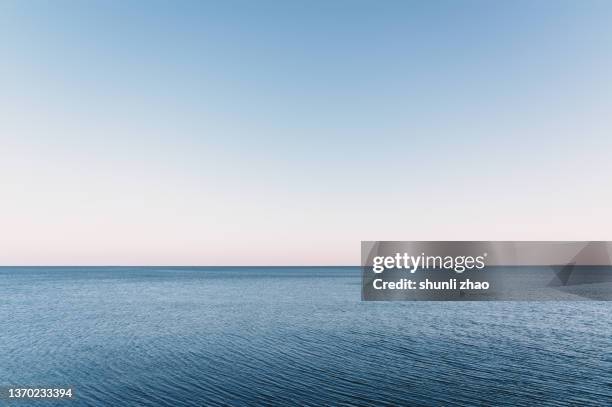 calm sea fading into the sky at dusk - blue sea photos et images de collection