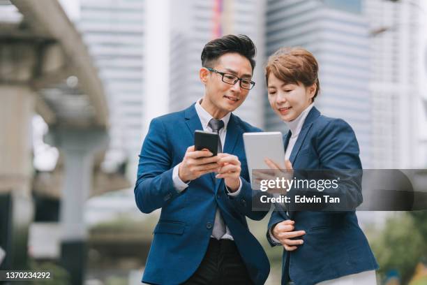 2 asian chinese colleague using digital tablet smart phone on city street - gedeelde mobiliteit stockfoto's en -beelden