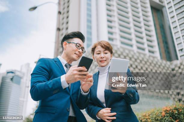 2 collega cinese asiatico che utilizza lo smartphone tablet digitale sulla strada della città - man suit using phone tablet foto e immagini stock