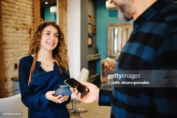 a beautician charging a customer for services using pos and smartphone - contactless paying - pago por móvil fotografías e imágenes de stock