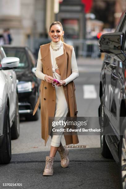 Olivia Palermo wears gold earrings, a gold large chain necklace, a white latte turtleneck long sleeves / cut-out chest / midi dress, a brown...