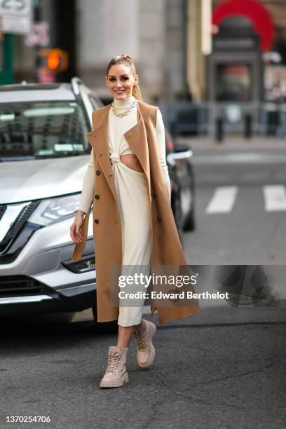 Olivia Palermo wears gold earrings, a gold large chain necklace, a white latte turtleneck long sleeves / cut-out chest / midi dress, a brown...