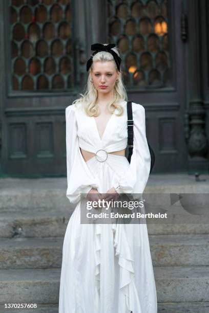 Avrey Ovard wears a black velvet knot headband, black sunglasses, silver earrings, a white pleated / V-neck / puffy sleeves / cut-out chest / ruffled...