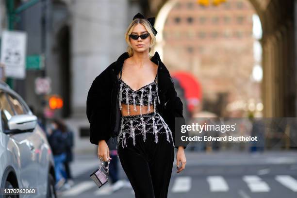 Guest wears black vintage sunglasses, a black velvet knot headband, a black velvet with embroidered pearls flower and fringed V-neck cropped top from...