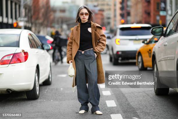 Guest wears beige sunglasses, gold chain pendant earrings, a black ribbed cut-out pullover, a brown suede with sheep interior oversized long coat, a...