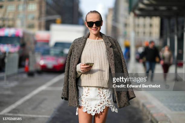 Guest wears sunglasses, a beige braided pullover, a black and beige striped print pattern blazer coat, a white cut-out pattern asymmetric short...