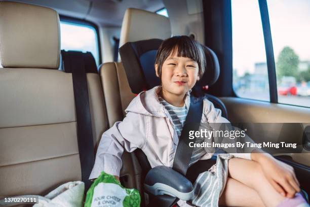 lovely little girl smiling joyfully at the camera while sitting in child car seat, enjoying her snack in the car - car back seat stock pictures, royalty-free photos & images