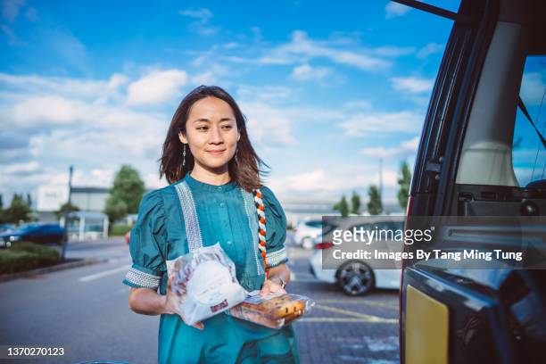 young asian woman putting some groceries in her car trunk after going shopping in supermarket - real people shopping stock pictures, royalty-free photos & images