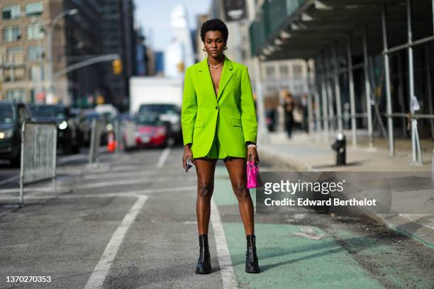 Guest wears gold large earrings, a gold large chain necklace, a green flashy blazer jacket, matching green flashy suit shorts, pearls bracelets,...