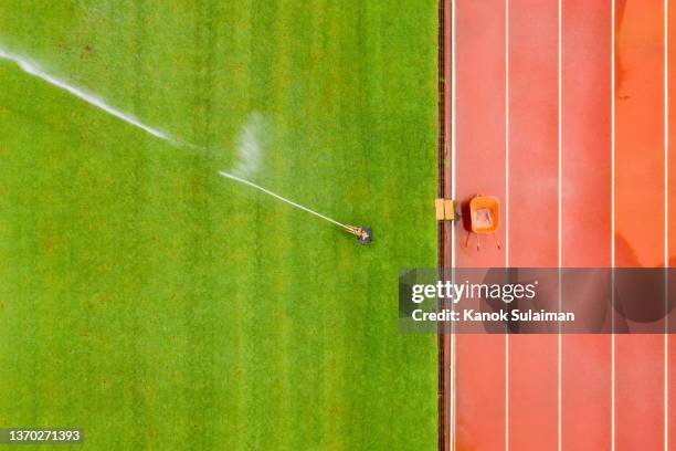 empty soccer field and running track with water sprinkler system on - estadio de atletismo fotografías e imágenes de stock