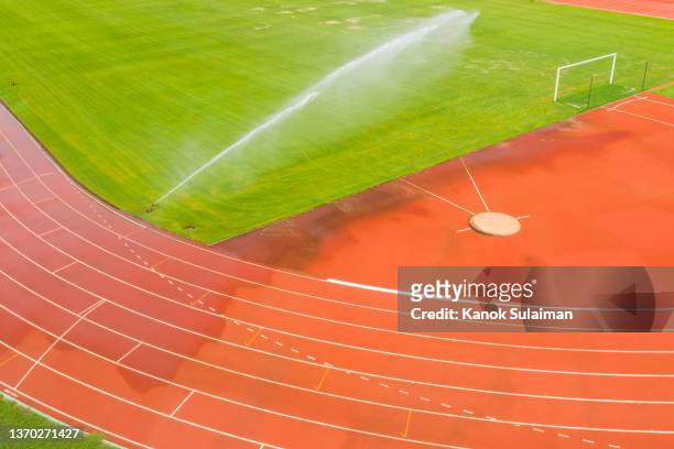 empty soccer field and running track with water sprinkler system on - 陸上競技場　無人 ストックフォトと画像