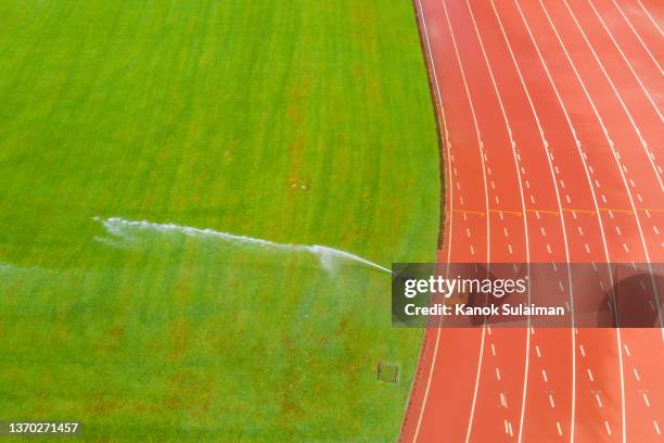 empty soccer field and running track with water sprinkler system on - 陸上競技場　無人 ストックフォトと画像